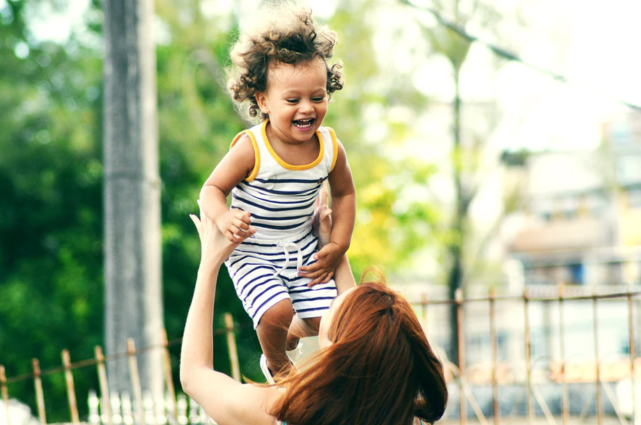 Mother holding young child up laughing | Life Insurance
